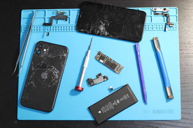 Opened phones, a battery and repair tools on a work mat